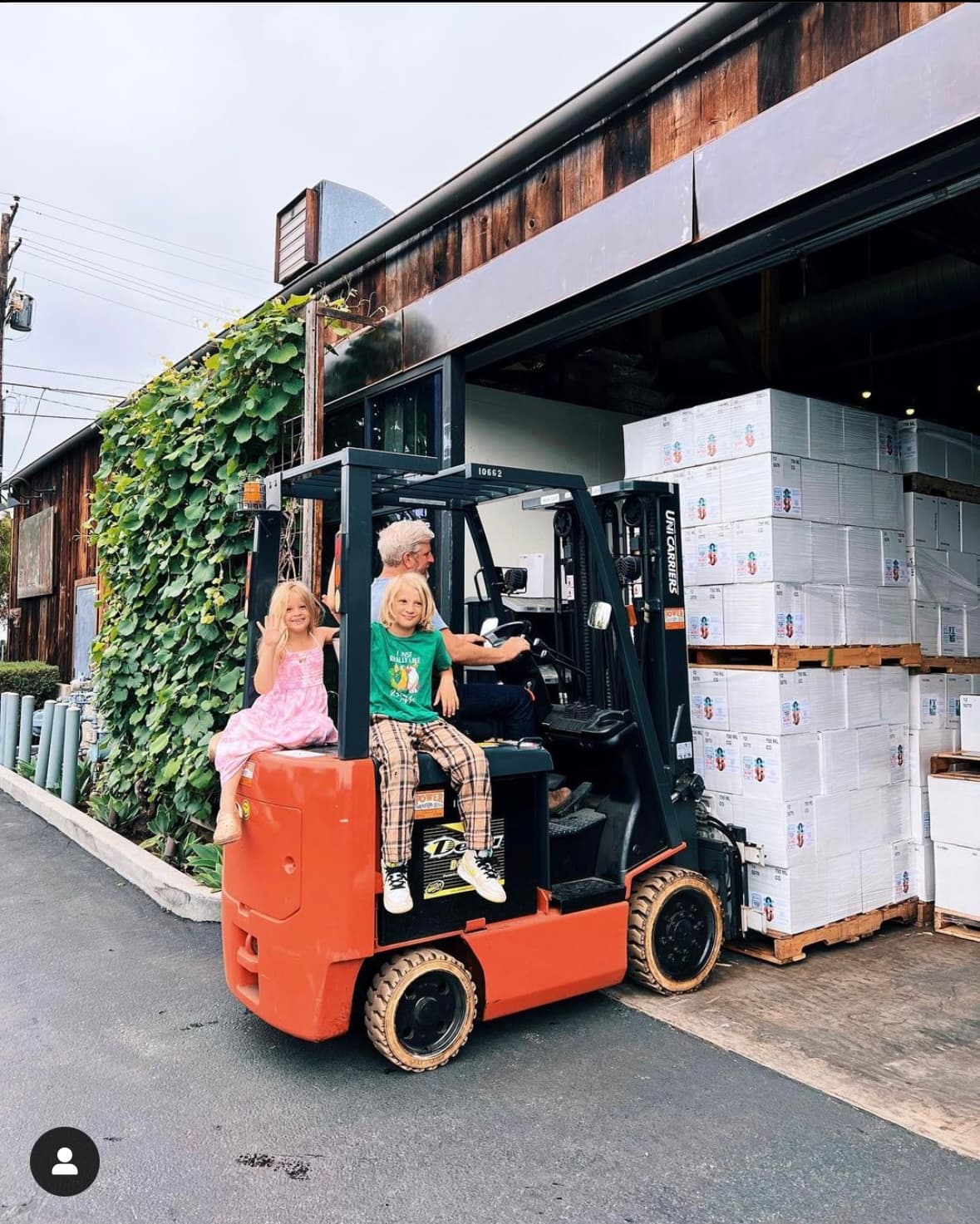 Dave Potter on a forklift outside the Municipal Winemakers warehouse, two kids riding along, pallets of finished cases stacked beside him